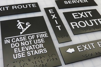 ADA-compliant exit route signs with braille and fire safety instructions, including arrows and pictograms, relevant to Sign East's signage services.