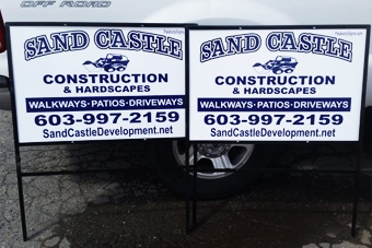 Construction signage for Sand Castle, featuring services like walkways, patios, and driveways, with contact details and website information.