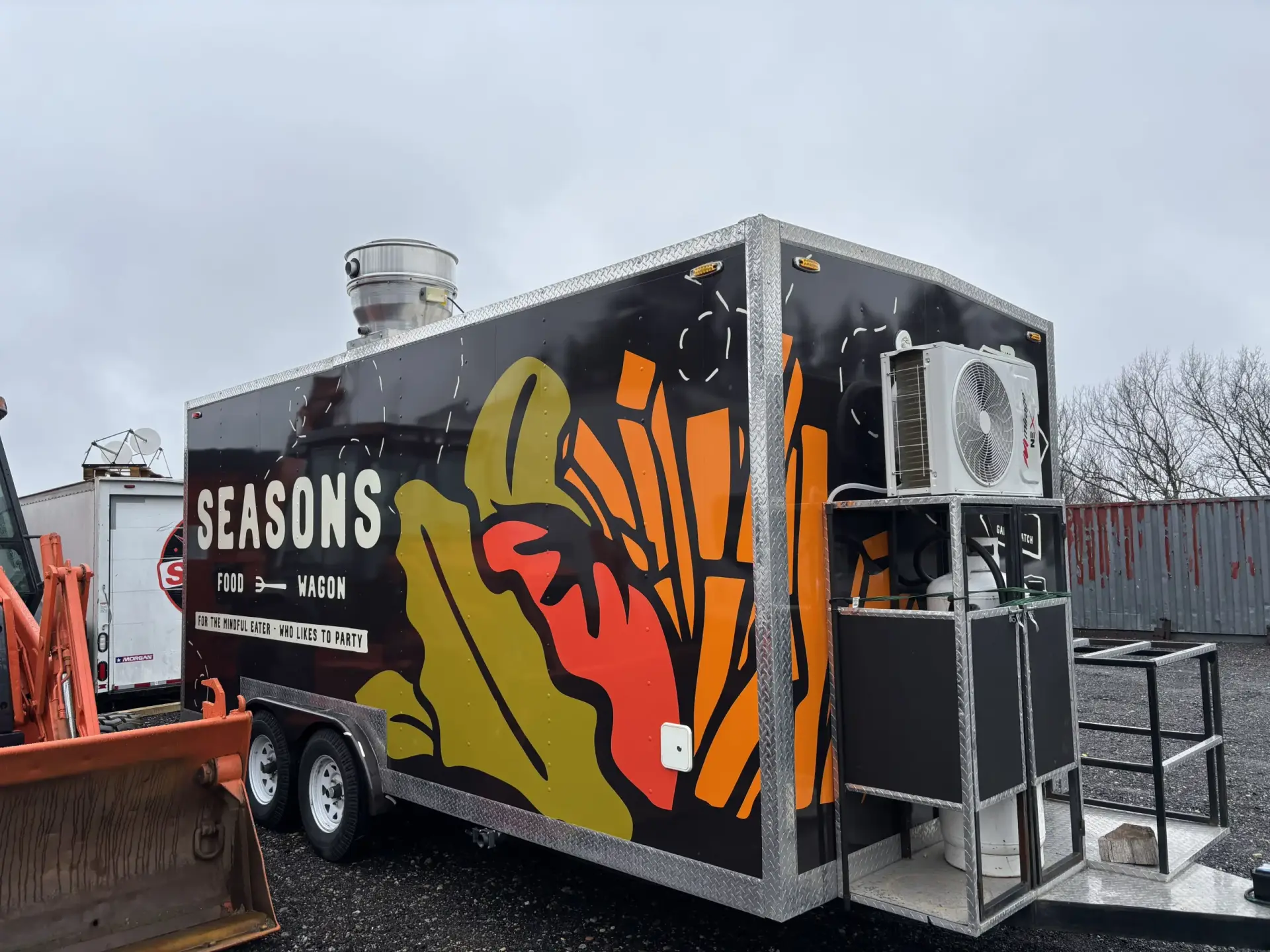 Food truck with vibrant "Seasons" branding, featuring colorful graphics of food items and equipped with an air conditioning unit, parked in a lot.