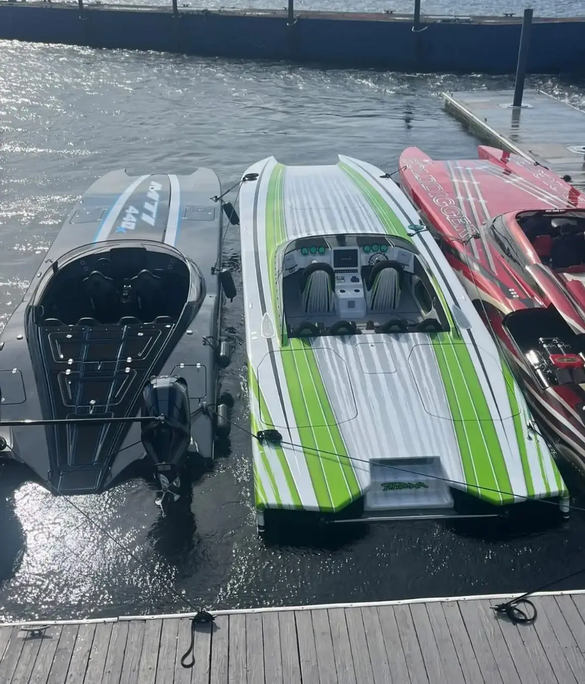 Three high-performance boats docked at a marina, featuring sleek designs in black, green, and red, showcasing premium marine-grade vinyl graphics for boat identification and branding.