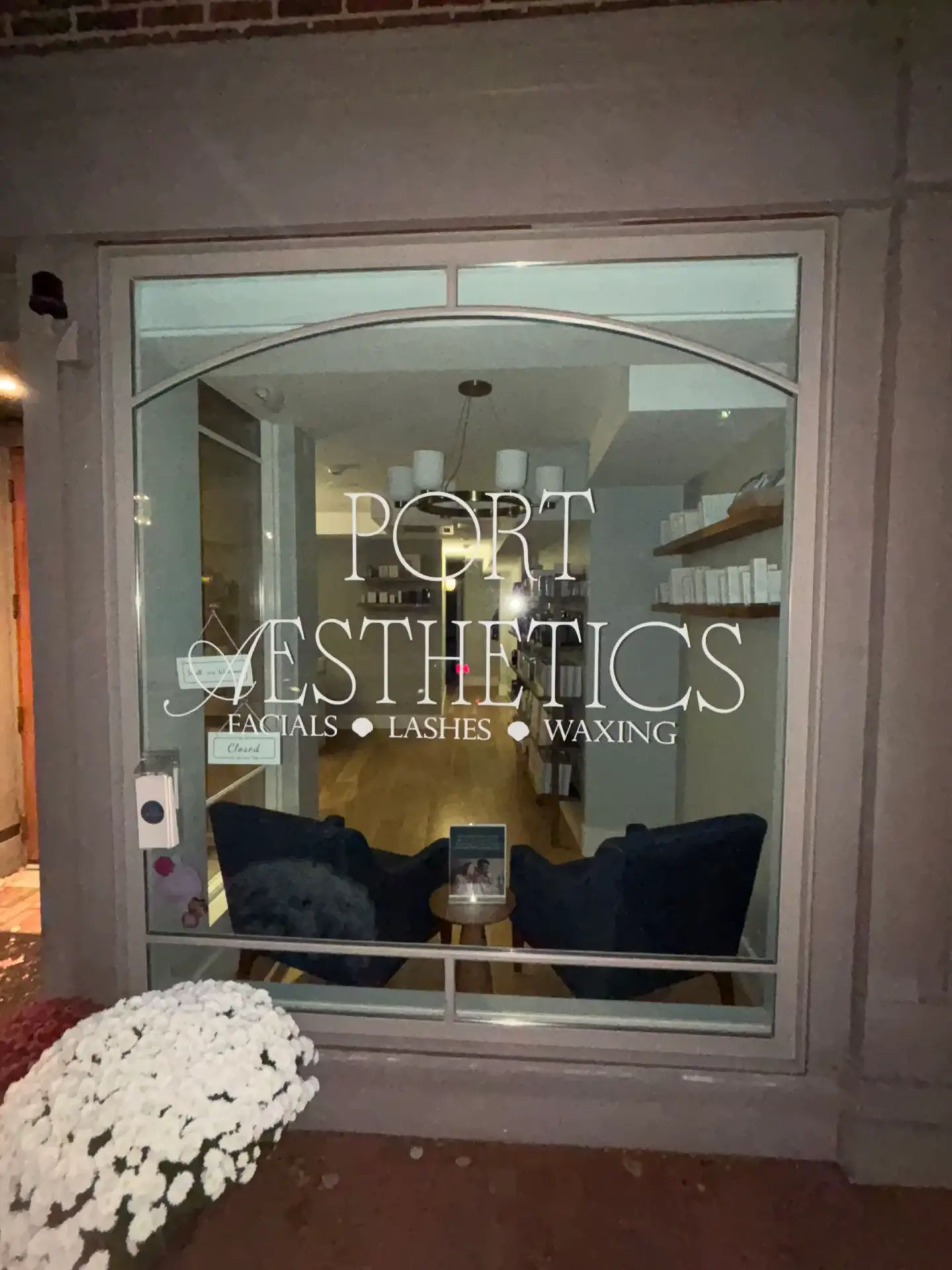 Port Aesthetics storefront featuring illuminated signage, with services listed as facials, lashes, and waxing, and a welcoming interior visible through the glass window.