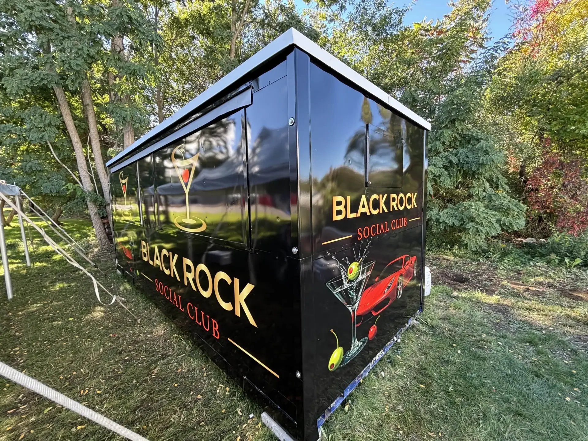 Black Rock Social Club branded trailer with cocktail graphics, set in a green outdoor environment, showcasing vibrant signage for Portsmouth businesses.