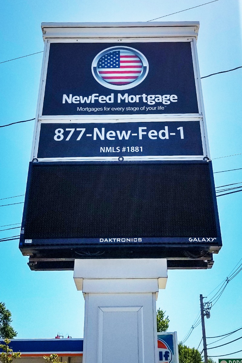 Illuminated sign for NewFed Mortgage featuring American flag logo, contact number, and tagline, showcasing visibility and branding for business.