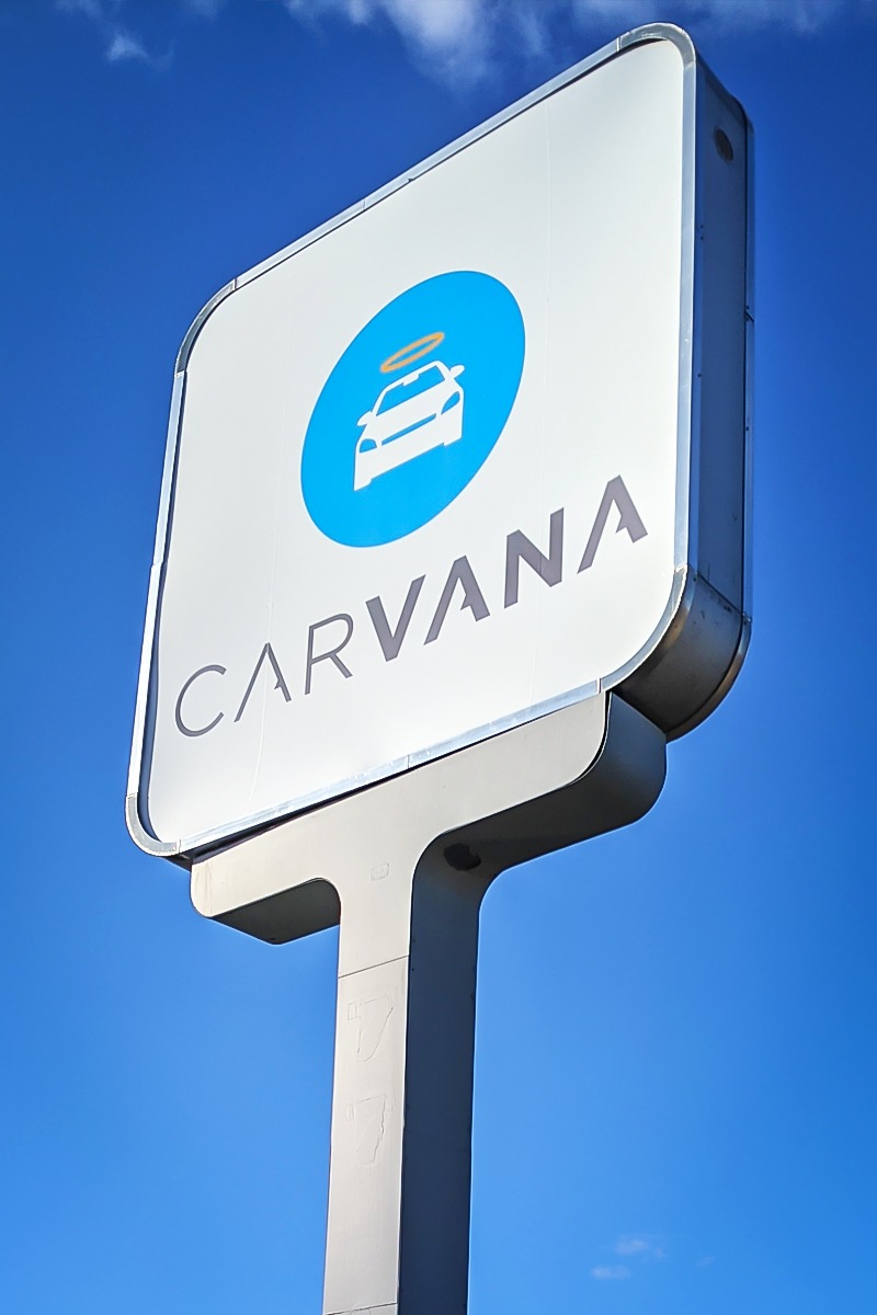 Illuminated sign for Carvana featuring a car icon and logo against a clear blue sky, showcasing custom design and visibility for businesses.