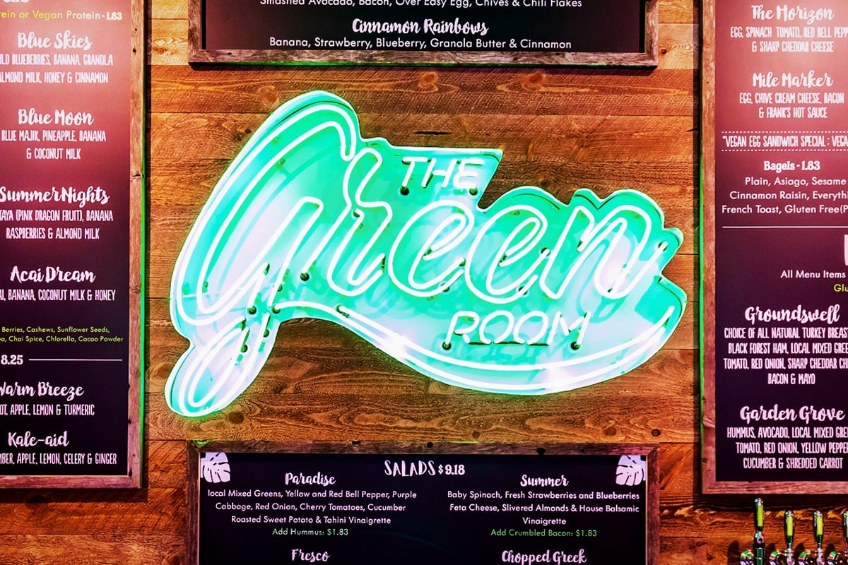 Neon sign reading "THE GREEN ROOM" glowing in turquoise and white, showcasing custom neon craftsmanship for a restaurant menu backdrop.
