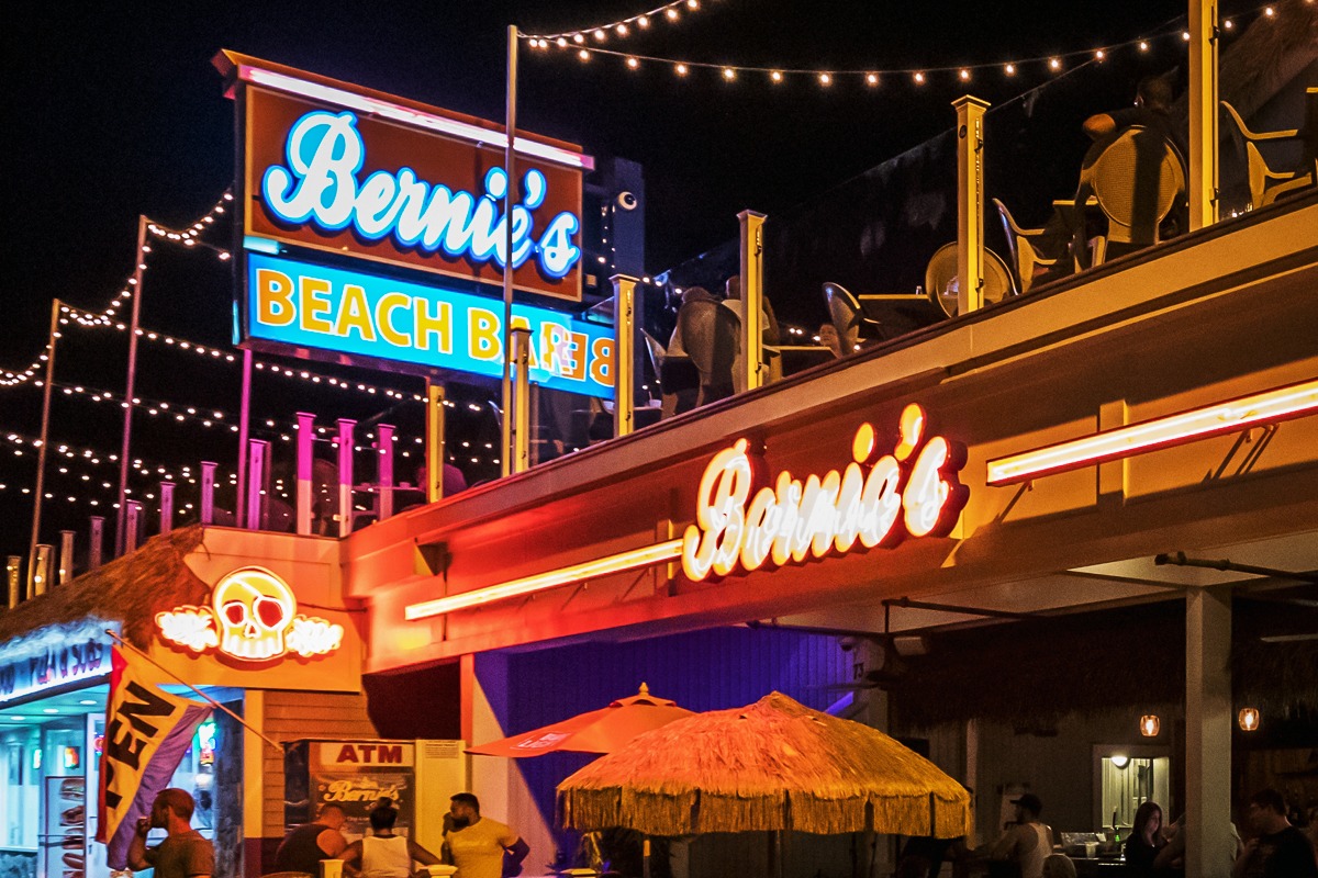 Neon sign for Bernie's Beach Bar illuminated at night, featuring vibrant colors and decorative string lights, showcasing the lively atmosphere of a beachside venue.