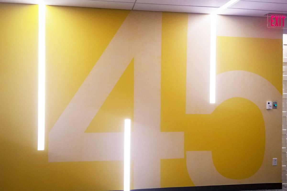 Yellow wall featuring large number "45" and modern lighting, showcasing custom wall graphics design by Signs East for office spaces.