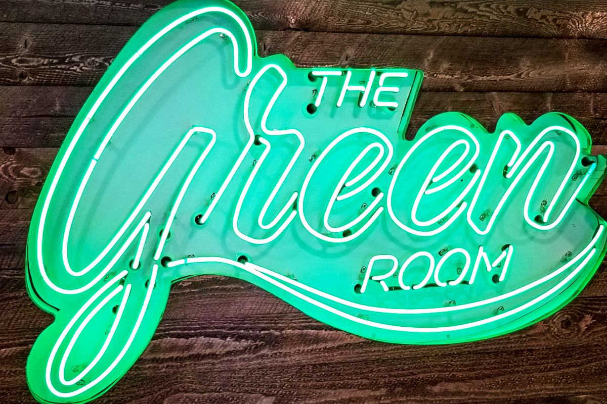 Neon sign reading "The Green Room" on wooden background, showcasing vibrant green and white colors, relevant to Sign East's illuminated sign services.