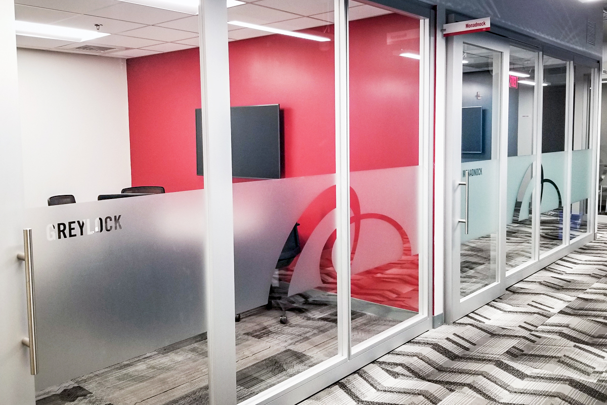 Frosted glass office door labeled "GREYLOCK" with modern design, featuring a red accent wall and visible seating area inside.