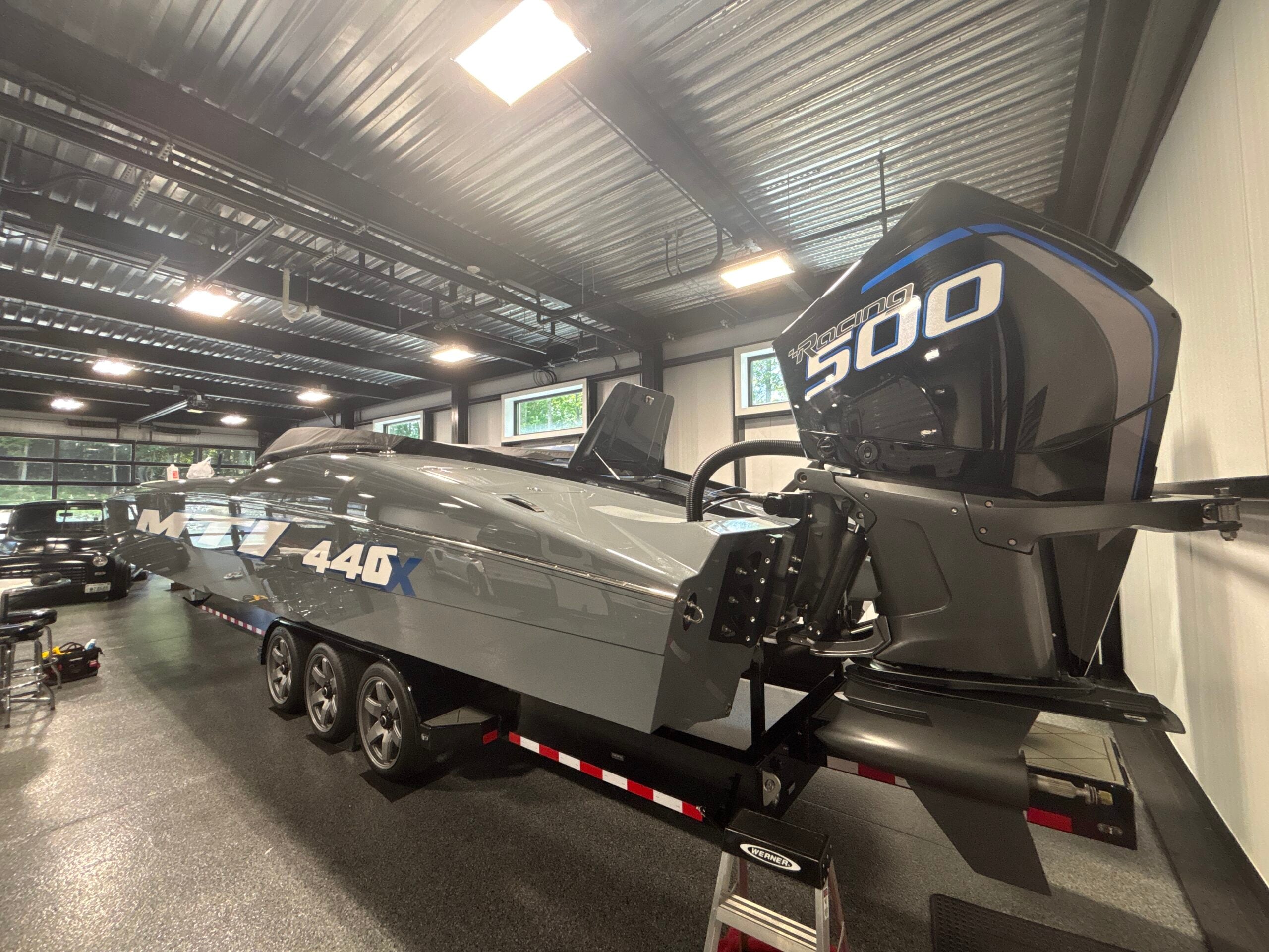 Custom boat with sleek gray hull featuring "440X" branding, mounted with a powerful "Racing 500" outboard motor, indoors in a well-lit facility.