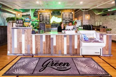 Custom floor graphic featuring "The Green Room" logo at a vibrant café counter, surrounded by plants and menu boards, illustrating branded messaging and promotional displays for customer engagement.