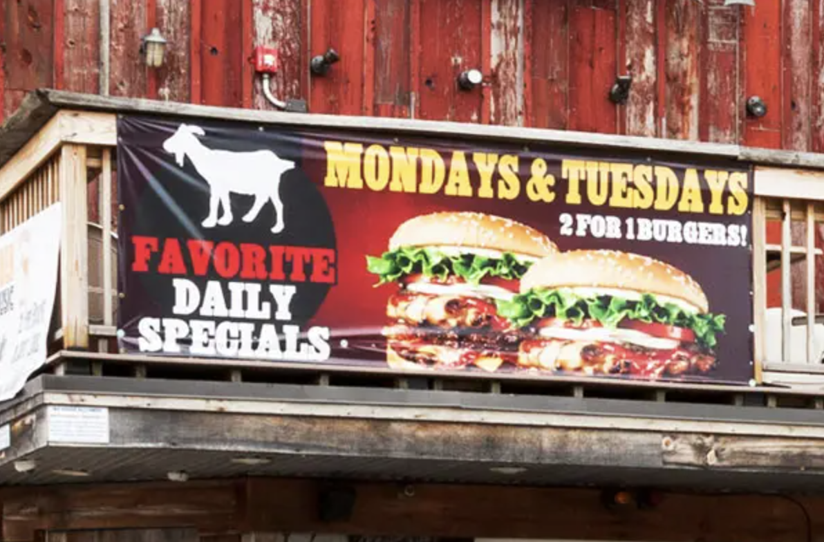 Banner advertising daily specials with images of burgers, featuring text "Mondays & Tuesdays 2 for 1 Burgers!" and "Favorite Daily Specials," set against a rustic wooden backdrop.