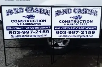 Construction signs for Sand Castle, featuring contact information and services like walkways, patios, and driveways, displayed prominently.