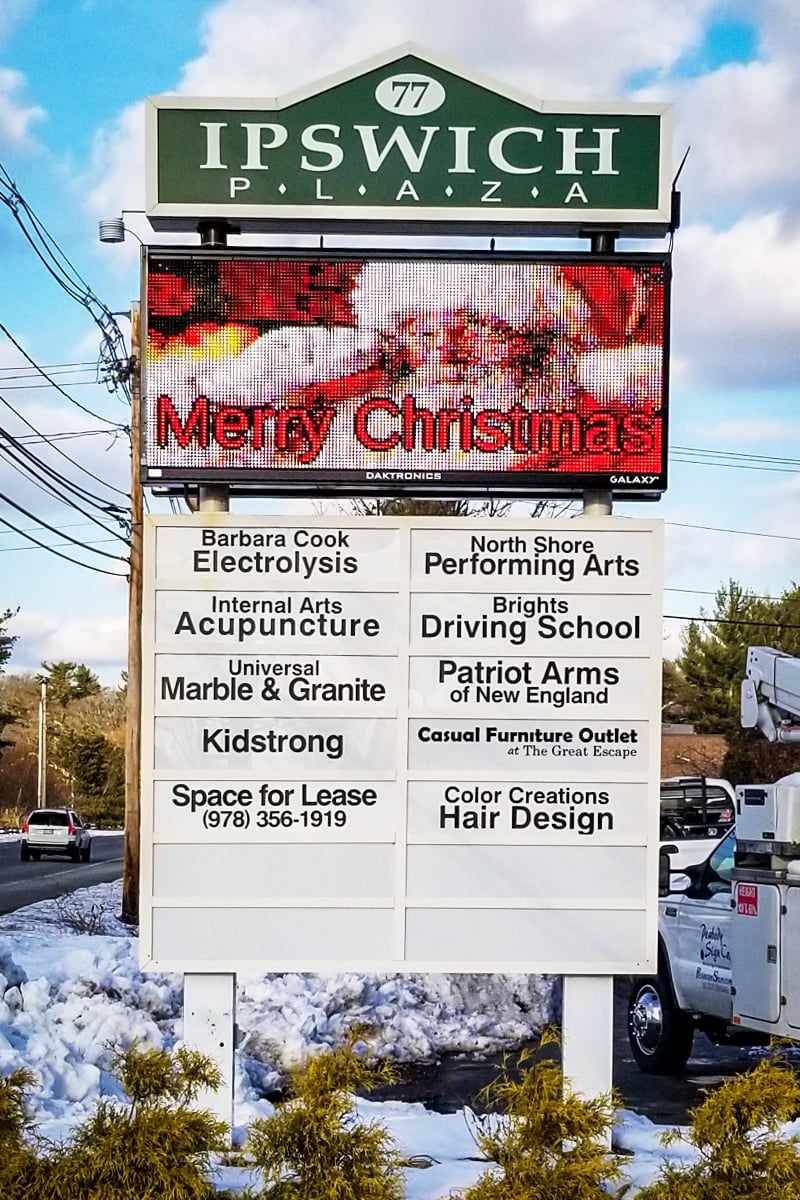 Multi-tenant pylon sign for Ipswich Plaza displaying "Merry Christmas" and tenant listings including Barbara Cook Electrolysis, Internal Arts Acupuncture, and others, showcasing illuminated and interchangeable panels for effective directory-style signage.
