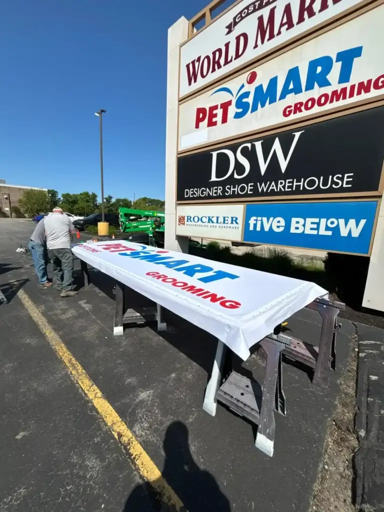 Sign installation for PetSmart Grooming on a storefront sign, featuring bold blue and red lettering, with workers preparing the sign in front of a shopping center.