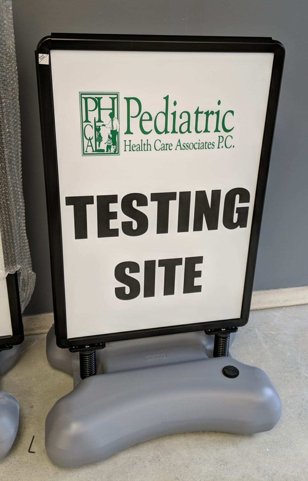 A-frame sidewalk sign displaying "Pediatric Health Care Associates P.C." and "TESTING SITE," designed for outdoor visibility and promoting healthcare services.