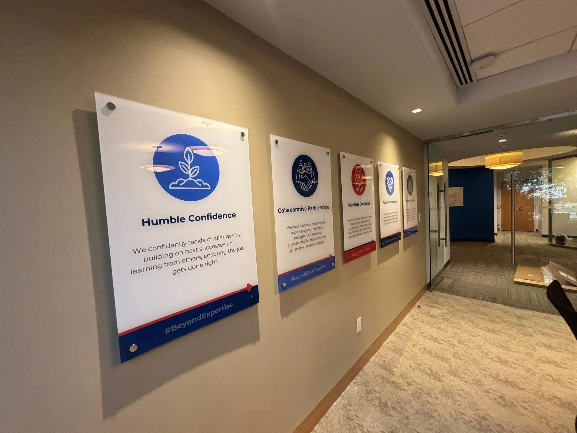Interior office signage displaying core values including "Humble Confidence," "Collaborative Partnerships," "Relentless Excellence," and "Relentless Innovation," with modern acrylic designs, promoting corporate identity and branding.