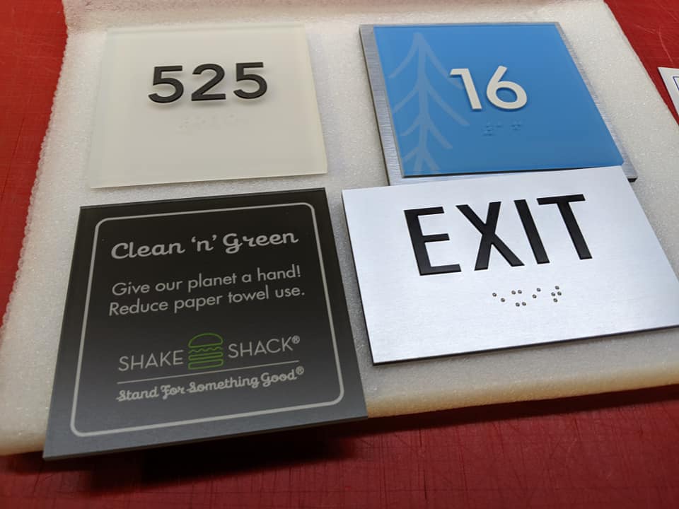 Acrylic signage samples including room numbers, directional signs, and eco-friendly messaging, showcasing custom designs for various applications.