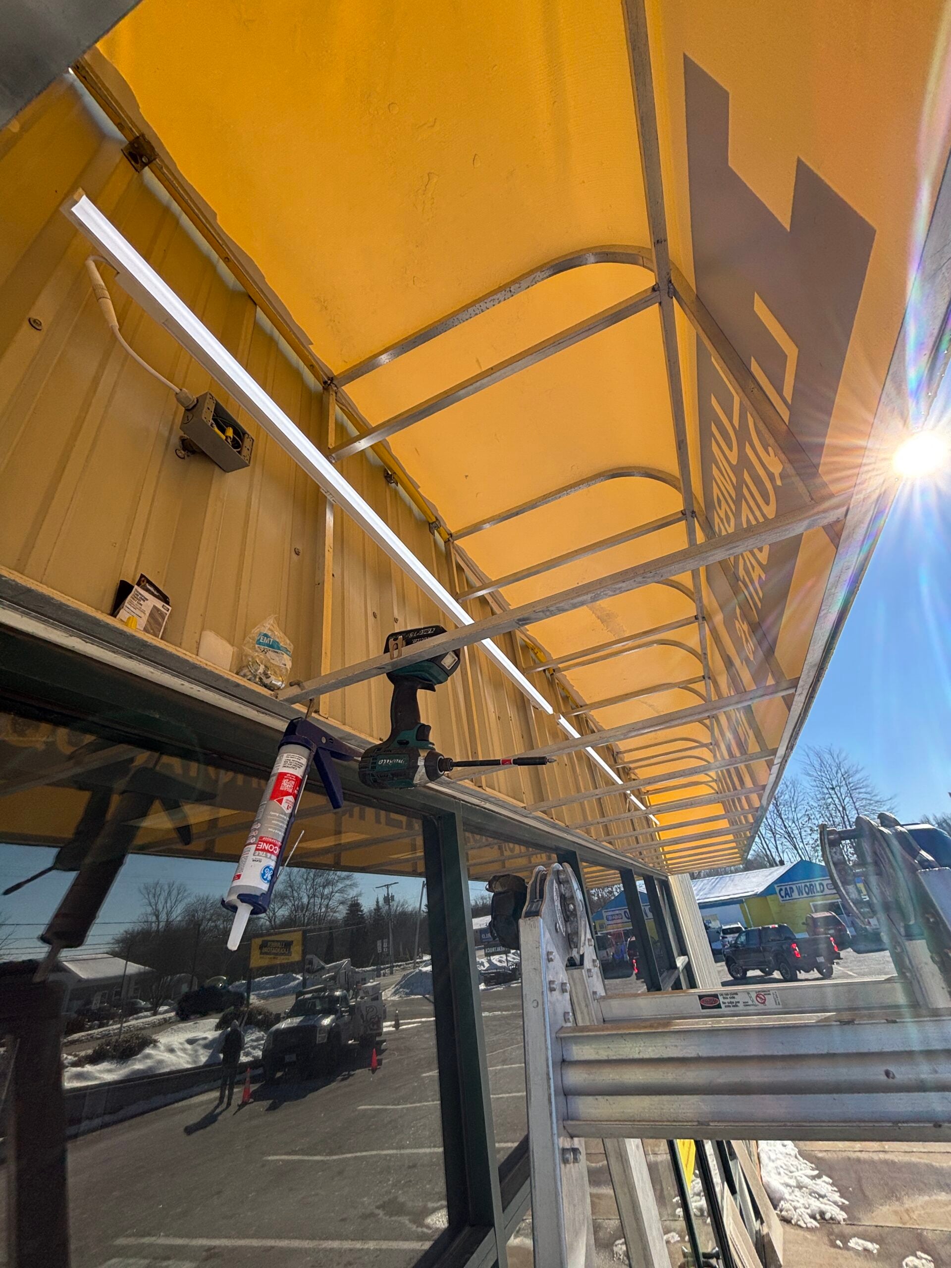 Awning installation in progress with retractable yellow awning, tools, and caulking visible, showcasing custom signage potential for outdoor dining and seasonal spaces.
