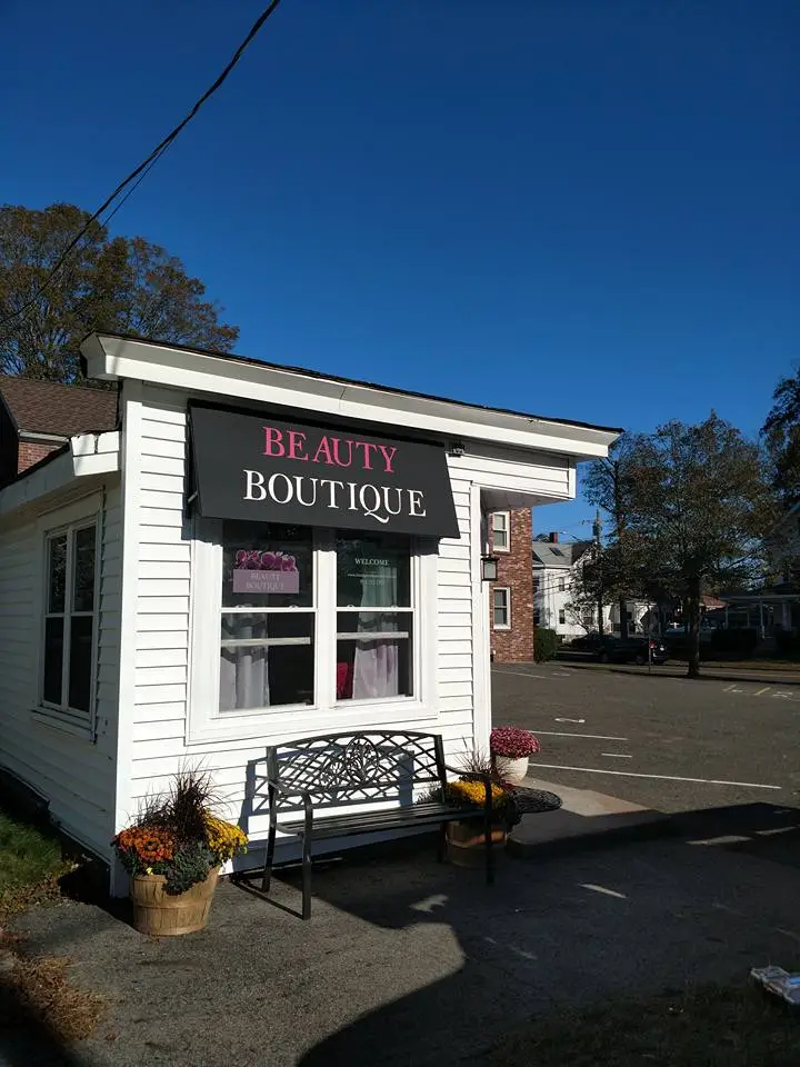 Beauty Boutique storefront featuring a custom awning sign with "BEAUTY BOUTIQUE" in bold pink letters, surrounded by potted flowers and a bench, showcasing a welcoming entrance for customers.