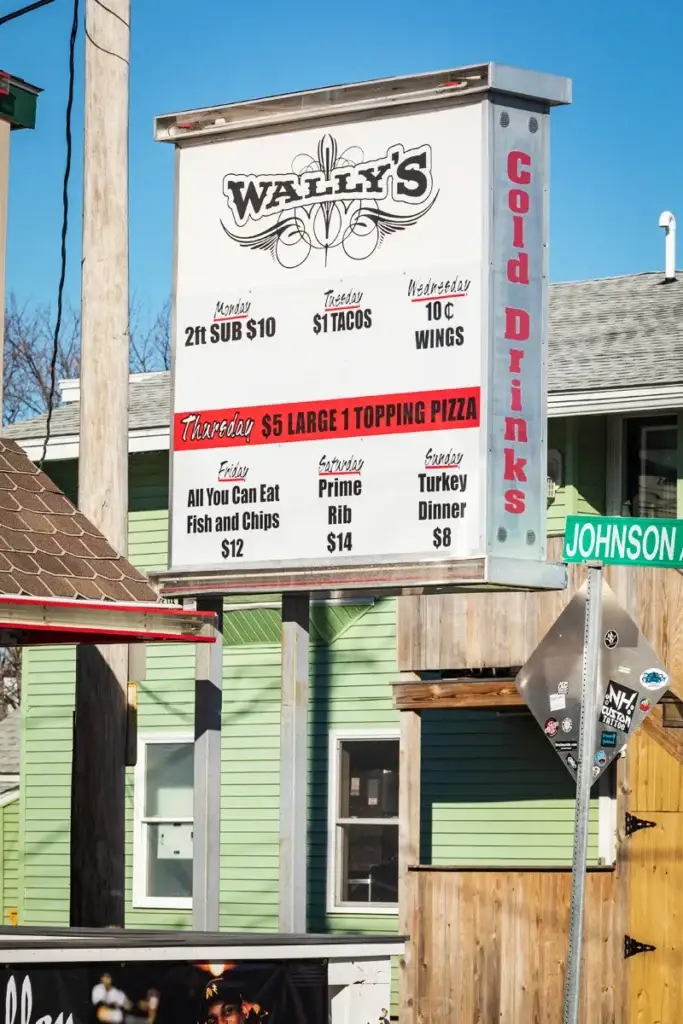 Wally's restaurant sign displaying daily specials, including $5 large one-topping pizza on Thursdays, surrounded by a vibrant neighborhood setting.