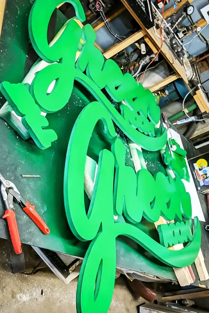 Green dimensional sign letters in a workshop setting, showcasing commercial sign design and fabrication process.