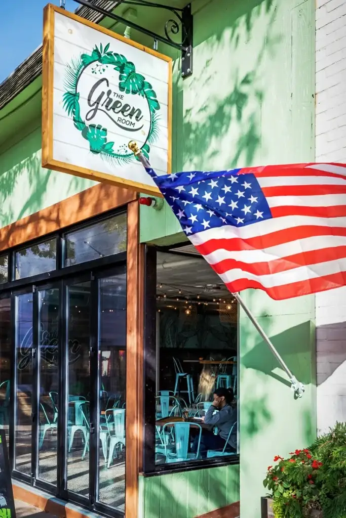 American flag waving outside a vibrant green café with tropical decor.