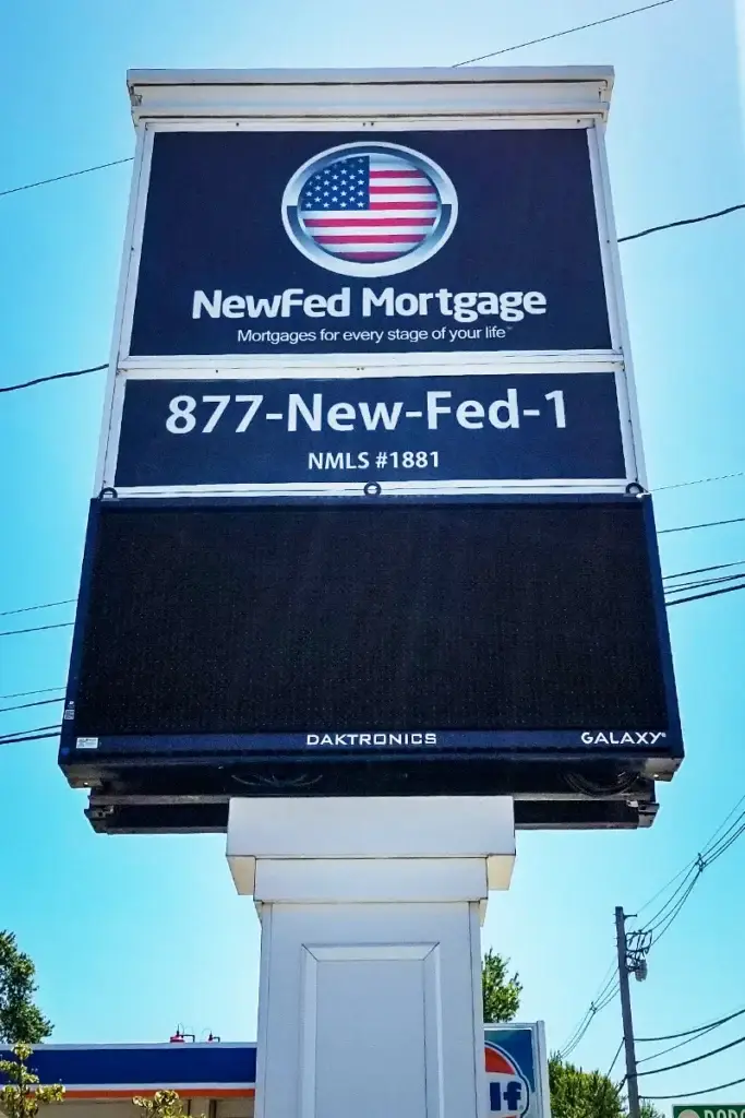 Sign for NewFed Mortgage featuring American flag logo, contact number, and tagline about mortgages, set against a clear blue sky.