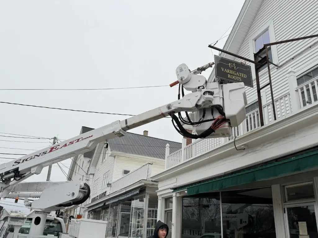 Bucket truck installing a sign for Variegated Roots on a storefront